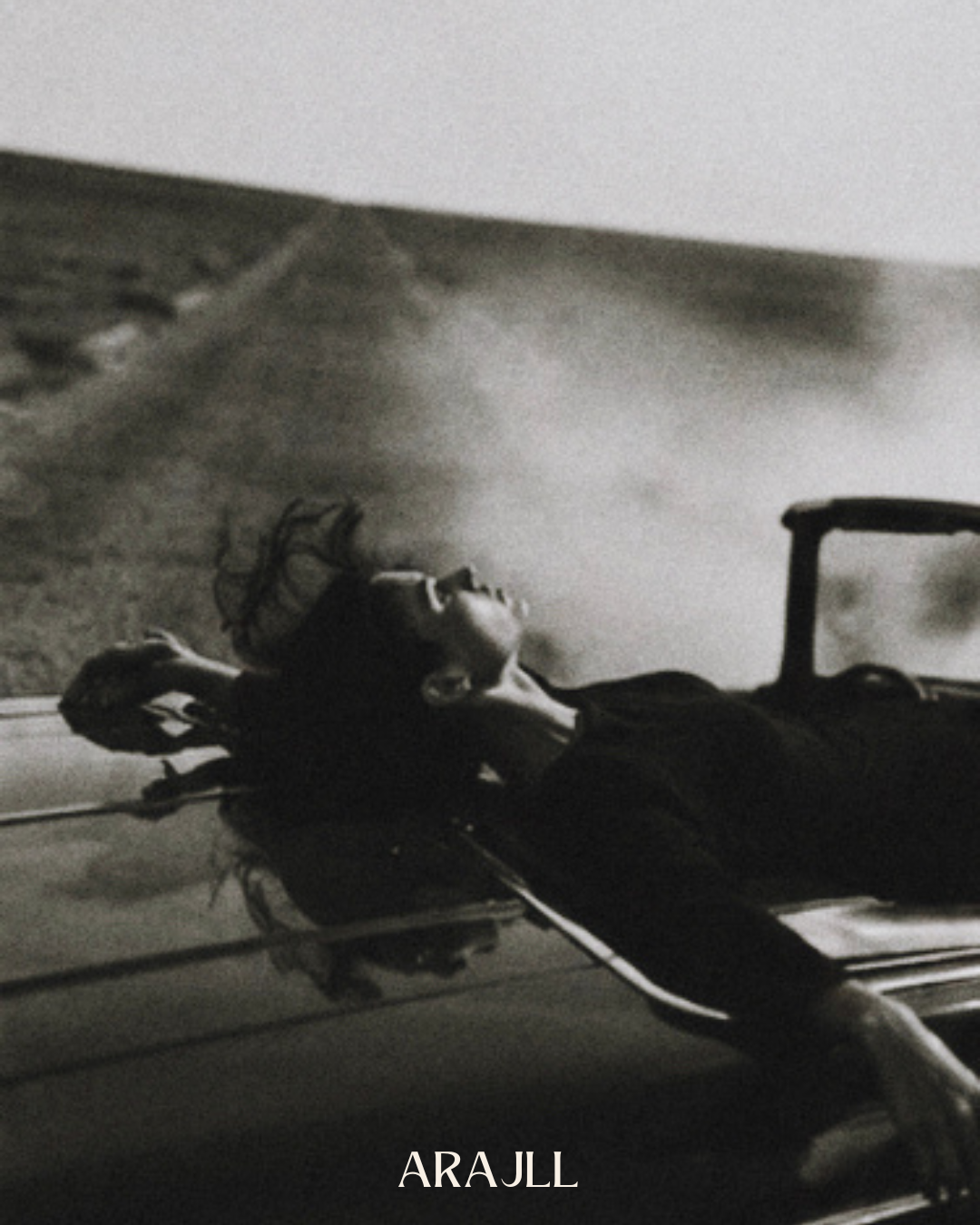Black and white photograph of a model leaning back across the bonnet of a vintage car, Black Dahlia campaign