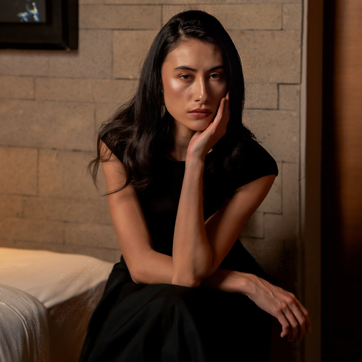 Model in a black dress seated with one hand resting against her face, Black Dahlia campaign